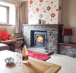A living room with a stone fireplace and a wooden chair with a red cushion at Haulfryn in Bethesda