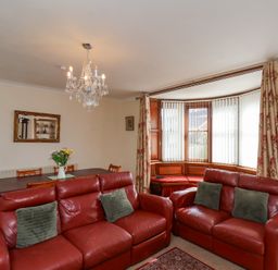 A living room with red leather sofas a dining table with flowers and a bay window with vertical blinds at Mayfield Manor in Whitby