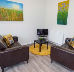 A living room with two brown leather sofas a small black table on a yellow rug a television and colorful paintings at Bramshurst in Upwey near Weymouth