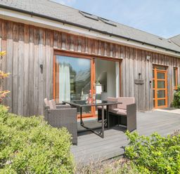 An outdoor patio with a wicker table and chairs in front of a wooden house at Bramshurst Upwey near Weymouth