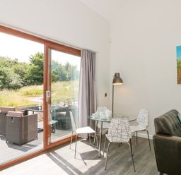 A dining area with a round glass table and four white chairs next to sliding glass doors showing an outdoor patio at Bramshurst in Upwey near Weymouth