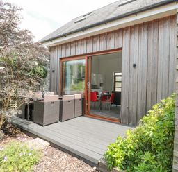 A wooden deck with outdoor seating and a table outside a house with sliding glass doors showing an interior dining area at Casterbridge in Upwey near Weymouth