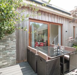 An outdoor patio area with a glass top table surrounded by six wicker chairs and a sliding glass door at Casterbridge in Upwey near Weymouth