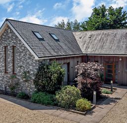 An exterior view of a house with a stone and wooden facade surrounded by plants and trees at Casterbridge Upwey near Weymouth