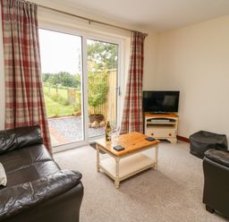 A living room with two brown leather sofas a wooden coffee table a television on a stand and glass sliding doors with red plaid curtains at Red Kite Cottage in Howey near Llandrindod Wells