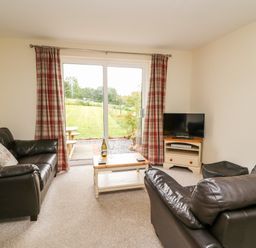 A living room with two leather sofas a wooden coffee table and a television with glass doors overlooking a garden at Red Kite Cottage in Howey near Llandrindod Wells