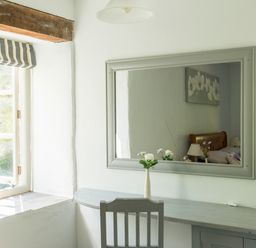 A room with a window a wall mirror a vase with flowers a chair and a desk at Mill Cottage in Hanley William near Tenbury Wells