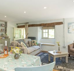 A living room with sofas a coffee table and a dining table with flowers and drinks at Mill Cottage in Hanley William near Tenbury Wells