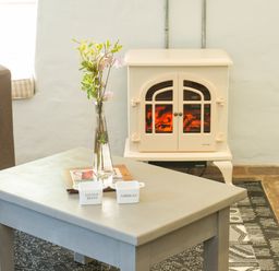 A room with a gray coffee table holding a glass vase with flowers and small containers near a beige stove and a brown sofa at Mill Cottage in Hanley William near Tenbury Wells