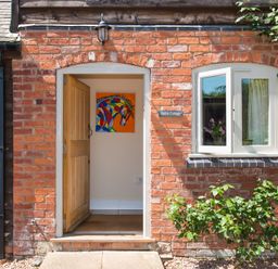 An open wooden door in a brick wall with a colorful horse painting inside at Stable Cottage Hanley William near Tenbury Wells