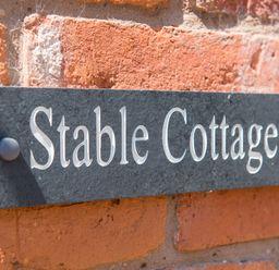 A close up of a black nameplate mounted on a brick wall with the text Stable Cottage