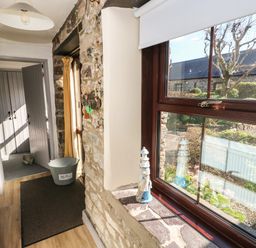 A hallway with a window showing a garden and a grey boot bin on the floor at Corner Cottage in Broad Haven