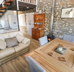 An open plan living area with a wooden dining table four chairs a cream sofa with cushions a wooden cabinet a wood burning stove and kitchen appliances at Corner Cottage in Broad Haven