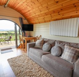 A living area with a sofa a dining table and chairs a television and large round doors opening to a patio at Valley View in Rhayader