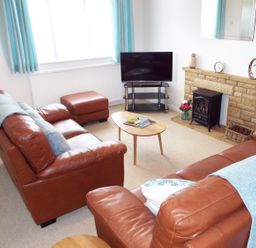 A living room with two brown leather sofas a small wooden coffee table a television on a stand and a fireplace at Kates Cottage in Bourton-on-the-Water