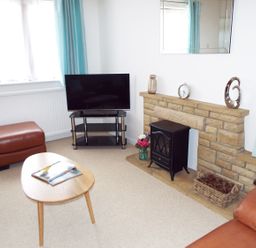 A living room with a television on a stand a leather ottoman a wooden coffee table and a stone fireplace at Kates Cottage in Bourton on the Water