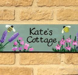 A painted sign with flowers and bees on a brick wall at Kates Cottage in Bourton-on-the-Water
