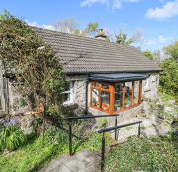 A stone cottage with a glass sunroom and tiled roof surrounded by greenery and flowers at Dun na Ron in Oughterard County Galway