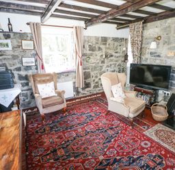 A living room with two armchairs a television stone walls and a red patterned carpet at Dun na Ron in Oughterard County Galway