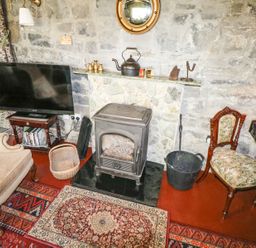 A room with a fireplace stove television armchair and wooden chair at Dun na Ron in Oughterard County Galway