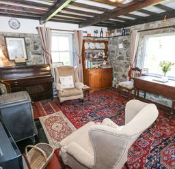 A sitting room with armchairs a piano a wooden cabinet a table with chairs and a stove at Dun na Ron in Oughterard County Galway