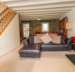 A living room with a leather sofa stair railing stone wall and a small window at Nantmel in Beddgelert