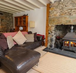 A living room with a leather sofa and cushions beside a stone fireplace with a wood burning stove at Nantmel in Beddgelert