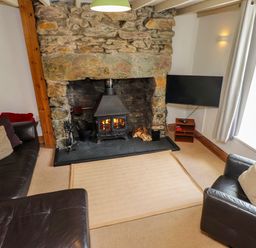 A living room with a stone fireplace wood burning stove two leather sofas a television on a stand and a window with curtains at Nantmel in Beddgelert