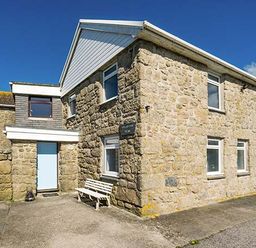 A stone house with multiple windows and a white bench outside at Tregiffian Vean in Sennen Cove