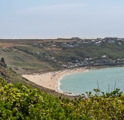 A beach with people and houses on a hillside at The Lookout in Sennen