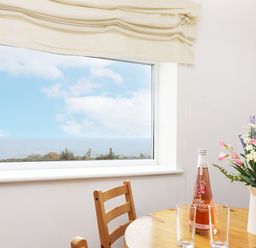 A dining room with a table, chairs, flowers, and a bottle of beverage at The Coach House in Sennen near St Just