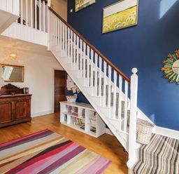 A staircase with striped carpet and blue wall with artwork and mirror in a hallway with wooden floor and a striped rug at Millers Lane House Muff County Donegal