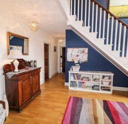 An entryway with wooden flooring a white staircase blue wall a wooden cabinet with a lamp and a white shelf with books at Millers Lane House Muff County Donegal