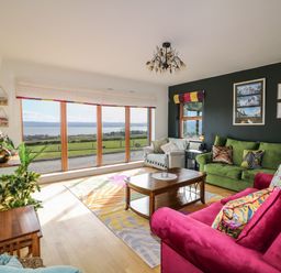 A living room with large windows showing a landscape with sofas a wooden coffee table and plants at Millers Lane House in Muff County Donegal