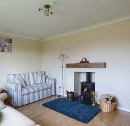A living room with a striped sofa wood burning stove and a blue rug at Skylark in Weybourne