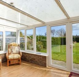 A sunroom with two wicker armchairs with cushions and glass doors opening to a garden at Skylark in Weybourne