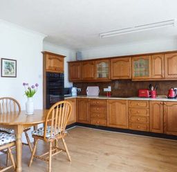 A kitchen with wooden cabinets a dining table with chairs and a vase of flowers at Skylark in Weybourne