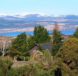 A view of trees and a small house with a lake and snow-covered mountains in the background at Pine Lodge in Culbokie