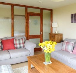 A living room with two sofas a wooden coffee table with flowers and a wooden cabinet at Pine Lodge in Culbokie