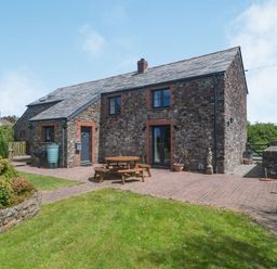 A stone house with a slate roof and outdoor seating area on a brick patio at Penbarden Barn in Dizzard near Crackington Haven