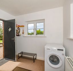 A utility room with a washing machine a shoe rack a coat rack an open black door and two windows at Penbarden Barn in Dizzard near Crackington Haven