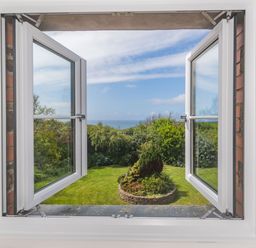 View through open white framed window onto garden with circular brick flower bed and trees at Penbarden Barn in Dizzard near Crackington Haven