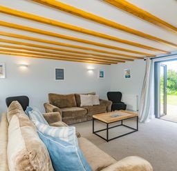 A living room with two sofas a coffee table and an open door leading outside at Penbarden Barn Dizzard near Crackington Haven