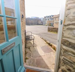 View through an open blue door with a sign The Dale Cottage showing a stone pathway and a metal bench outside at The Dale Cottage in Allendale near Hexham