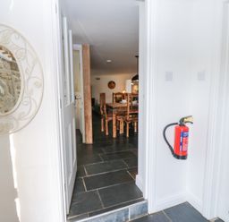 Hallway with a fire extinguisher mounted on the wall and a round mirror with decorative frame next to a doorway leading to a dining area with wooden chairs at The Dale Cottage in Allendale near Hexham