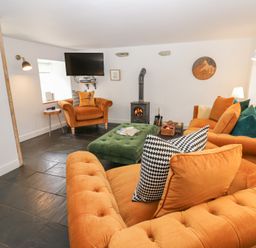 A living room with orange sofas green ottoman wood stove and a wall-mounted TV at The Dale Cottage in Allendale near Hexham