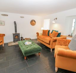 A living room with orange sofas a green ottoman a wood burning stove and a television at The Dale Cottage in Allendale near Hexham