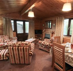 A living room with floral and striped sofas a dining table set for four and wooden walls at Sycamore Lodge in Liverton near Danby