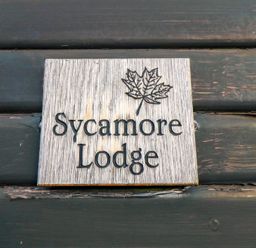 A wooden sign with a leaf and the text Sycamore Lodge on a dark wooden wall at Sycamore Lodge in Liverton near Danby
