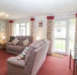 A living room with sofas a glass dining table and curtains at Sycamores Rosecraddoc Lodge near Liskeard